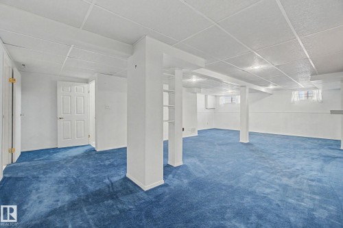 Spacious finished basement featuring blue carpeting, white walls, multiple support columns, built-in shelving, and recessed lighting - 1542 54 Street, Edmonton, AB - Indoor