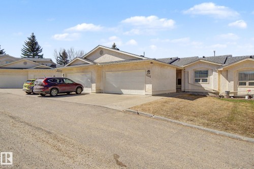 Single-story stucco exterior residence featuring an attached garage with a white overhead door, multiple windows, and a paved driveway - 1542 54 Street, Edmonton, AB - Outdoor