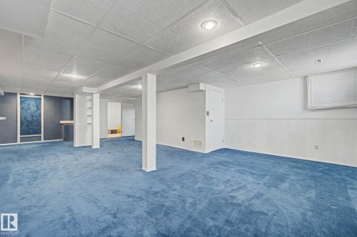 Spacious room featuring blue carpeting, white walls with a chair rail, a drop ceiling with recessed lighting, and support columns - 1542 54 Street, Edmonton, AB - Indoor