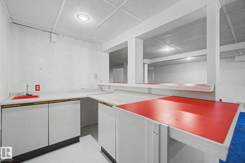 Finished basement space featuring a built-in bar area with wrap-around white cabinetry and red countertop surfaces - 1542 54 Street, Edmonton, AB - Indoor