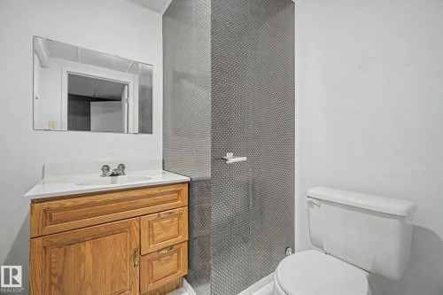 Bathroom featuring a wood-finish vanity with a white countertop and integrated sink, chrome faucet, and a large wall-mounted mirror - 1542 54 Street, Edmonton, AB - Indoor Photo Showing Bathroom