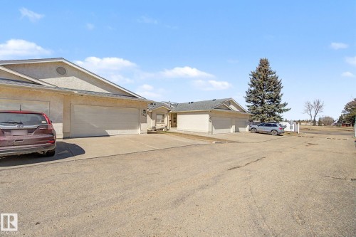 Exterior stucco finish with multiple attached garages, concrete driveways, and a mature evergreen tree - 1542 54 Street, Edmonton, AB - Outdoor