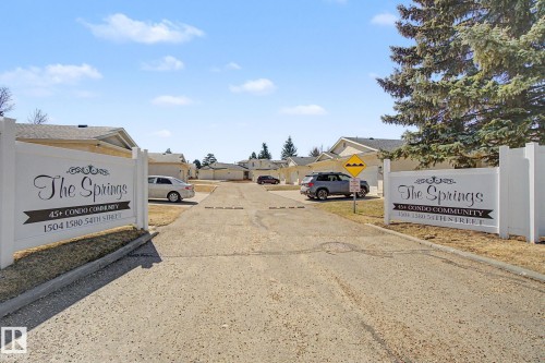 Entrance to "The Springs," a condo community featuring a white vinyl fence and a paved roadway - 1542 54 Street, Edmonton, AB - Outdoor