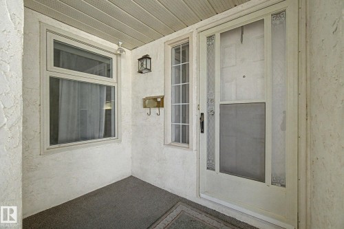 Covered entry with textured stucco walls, dual-pane window, decorative outdoor lantern, and a storm door featuring a screen panel - 1542 54 Street, Edmonton, AB - Outdoor With Exterior