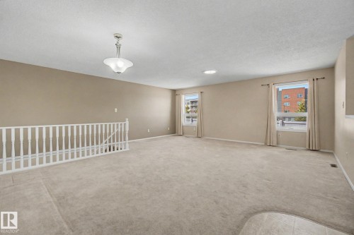 Spacious living area featuring neutral carpeting, light beige wall paint, multiple windows, a ceiling-mounted light fixture, and a white balustrade - 1542 54 Street, Edmonton, AB - Indoor Photo Showing Other Room