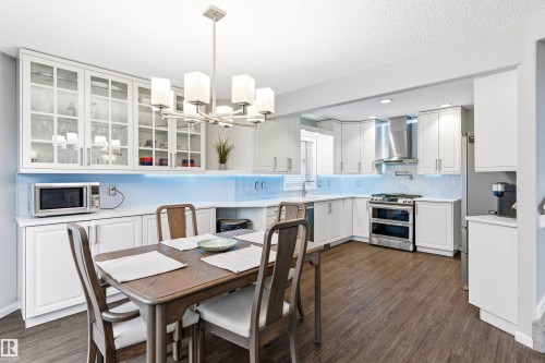 Open-concept kitchen and dining area featuring wood-finish flooring, white cabinetry, stainless steel appliances, and a tiled backsplash - 14755 131 Street Nw, Edmonton, AB - Indoor Photo Showing Dining Room
