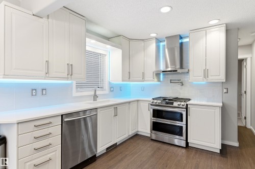 Contemporary kitchen featuring white cabinetry, stainless steel appliances, white subway tile backsplash, recessed lighting, and wood-finish flooring - 14755 131 Street Nw, Edmonton, AB - Indoor Photo Showing Kitchen