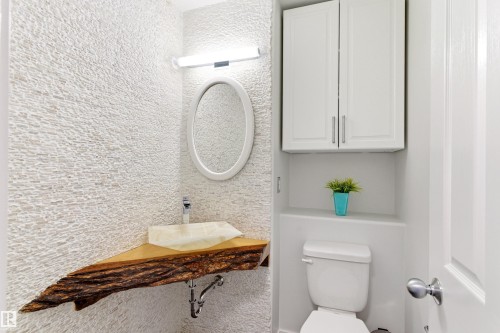 Bathroom featuring a live-edge wood vanity with a vessel sink, textured wall tile, wall-mounted oval mirror, and overhead lighting - 14755 131 Street Nw, Edmonton, AB - Indoor Photo Showing Bathroom