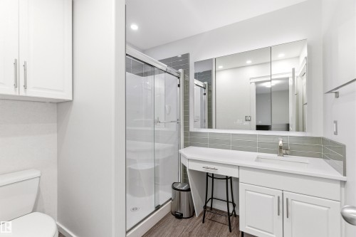 Modern bathroom featuring a glass-enclosed shower, white vanity with integrated sink, wood-finish flooring, a three-panel mirrored medicine cabinet, and white upper cabinetry - 14755 131 Street Nw, Edmonton, AB - Indoor Photo Showing Bathroom
