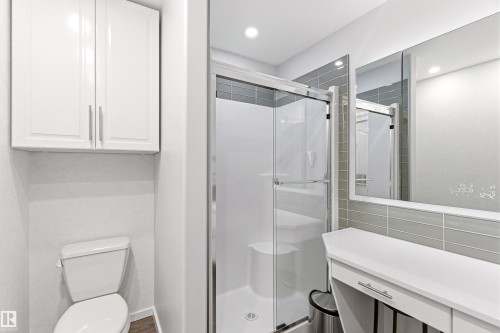 Modern bathroom featuring a glass-enclosed shower with sliding doors, white wall-mounted cabinetry, a built-in vanity with a drawer, and recessed lighting - 14755 131 Street Nw, Edmonton, AB - Indoor Photo Showing Bathroom