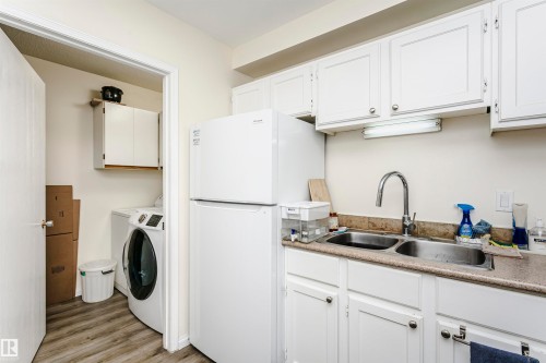 Utility area featuring a double basin stainless steel sink, white cabinetry, a built-in refrigerator, and wood-finish flooring - 303 10026 112 Street, Edmonton, AB - Indoor Photo Showing Laundry Room