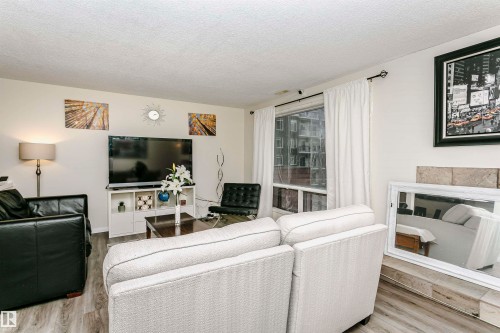 Living area featuring wood-finish flooring, a large window with white drapery, and a wall-mounted media console - 303 10026 112 Street, Edmonton, AB - Indoor Photo Showing Living Room