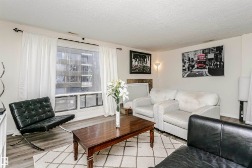 Living area featuring wood-finish flooring and a large window with white curtains - 303 10026 112 Street, Edmonton, AB - Indoor Photo Showing Living Room