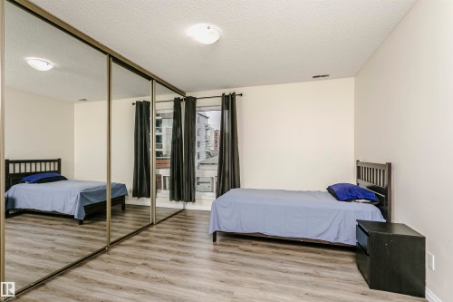 Spacious room featuring mirrored sliding closet doors, wood-finish flooring, and large windows with dark drapes - 303 10026 112 Street, Edmonton, AB - Indoor Photo Showing Bedroom