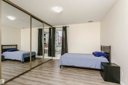 Spacious room featuring mirrored sliding closet doors, wood-finish flooring, and large windows with dark drapes - 