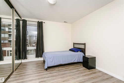 Spacious room with wood-finish flooring, a full-wall mirrored closet, and a large window - 303 10026 112 Street, Edmonton, AB - Indoor Photo Showing Bedroom