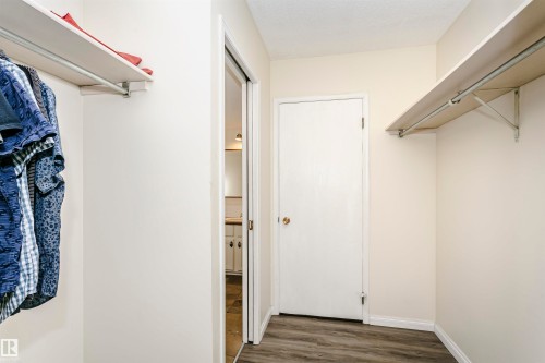 Walk-in closet featuring wood-finish flooring, white walls, built-in shelving, and hanging rods - 303 10026 112 Street, Edmonton, AB - Indoor