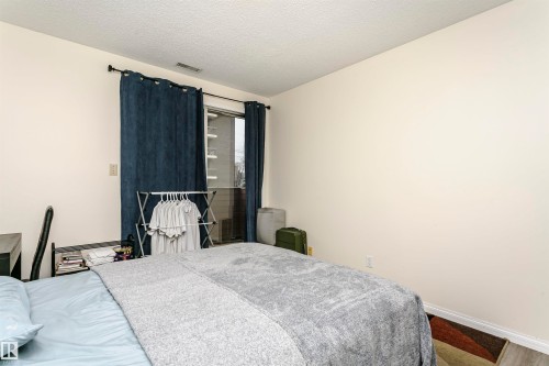 Room featuring a sliding glass door with dark fabric curtains, light-colored walls, and a textured ceiling - 303 10026 112 Street, Edmonton, AB - Indoor Photo Showing Bedroom