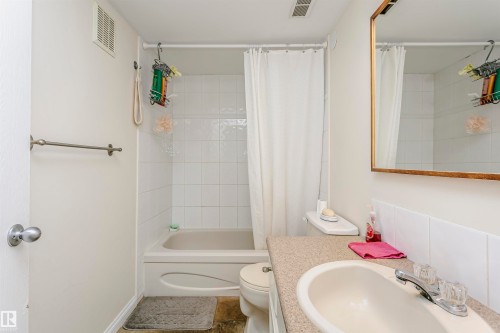 Bathroom featuring a bathtub with white tile surround, a built-in vanity with a composite countertop and integrated sink, and a wall-mounted mirror with a gold-tone frame - 303 10026 112 Street, Edmonton, AB - Indoor Photo Showing Bathroom