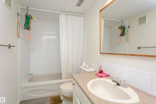 Bathroom featuring a built-in tub with white tile surround, a vanity with an integrated sink and laminate countertop, and a wall-mounted mirror with a wood-finish frame - 303 10026 112 Street, Edmonton, AB - Indoor Photo Showing Bathroom