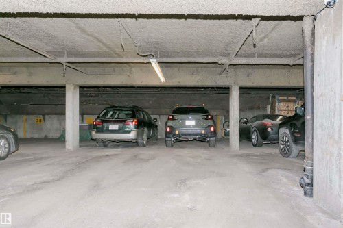 Underground parking garage featuring concrete flooring, exposed overhead piping, and fluorescent lighting fixtures - 303 10026 112 Street, Edmonton, AB - Indoor Photo Showing Garage