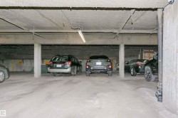 Underground parking garage featuring concrete flooring, exposed overhead piping, and fluorescent lighting fixtures - 