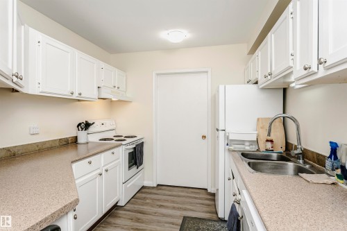 Kitchen featuring white cabinetry, speckled countertops, and wood-finish flooring - 303 10026 112 Street, Edmonton, AB - Indoor Photo Showing Kitchen With Double Sink