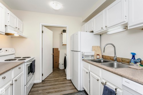 Efficient kitchen featuring wood-finish flooring, white cabinetry, a double basin stainless steel sink, and a white electric range with an overhead exhaust fan - 303 10026 112 Street, Edmonton, AB - Indoor Photo Showing Kitchen With Double Sink