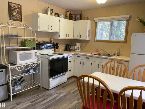 Kitchen featuring white cabinetry, a built-in window over the sink, and wood-finish flooring - 650031 Range Road 185, Rural Athabasca County, AB 