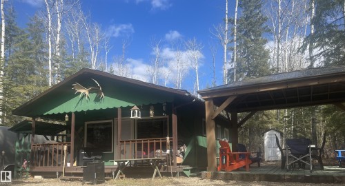 Exterior featuring a covered porch with wood railings, a secondary covered patio area, and a backdrop of mature trees - 650031 Range Road 185, Rural Athabasca County, AB 