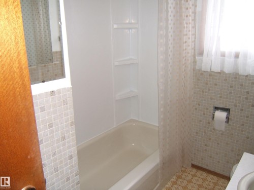 Bathtub with integrated shelving, patterned floor tiles, and a window with sheer curtain - 5030 52 Avenue, Andrew, AB - Indoor Photo Showing Bathroom