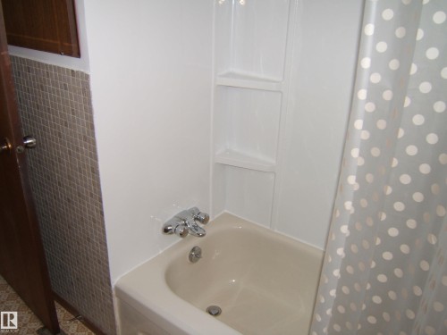 White bathtub with chrome fixtures and integrated shelving - 5030 52 Avenue, Andrew, AB - Indoor Photo Showing Bathroom