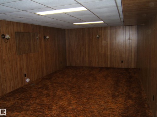 Spacious room featuring wood-finish paneling, a drop ceiling with integrated fluorescent lighting, and wall-mounted sconces - 5030 52 Avenue, Andrew, AB - Indoor
