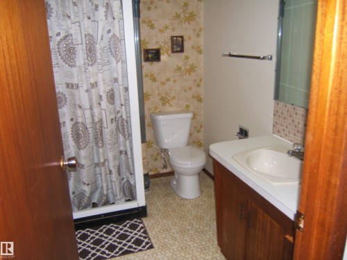 Bathroom featuring a single vanity with a laminate countertop, integrated sink, and wood-finish cabinetry - 5030 52 Avenue, Andrew, AB - Indoor Photo Showing Bathroom