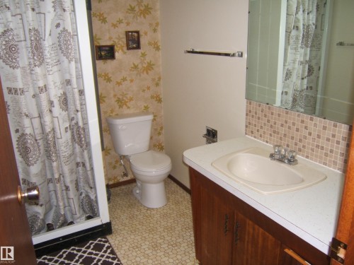 Bathroom featuring a single vanity with an integrated sink, mosaic tile backsplash, and a wall-mounted mirror - 5030 52 Avenue, Andrew, AB - Indoor Photo Showing Bathroom