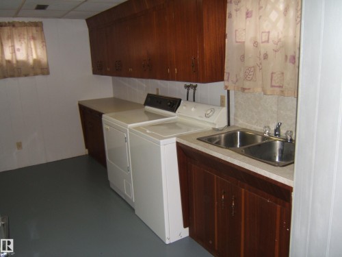 Utility room featuring wood-finish cabinetry, white wall paneling, and a dual basin stainless steel sink - 5030 52 Avenue, Andrew, AB - Indoor Photo Showing Laundry Room