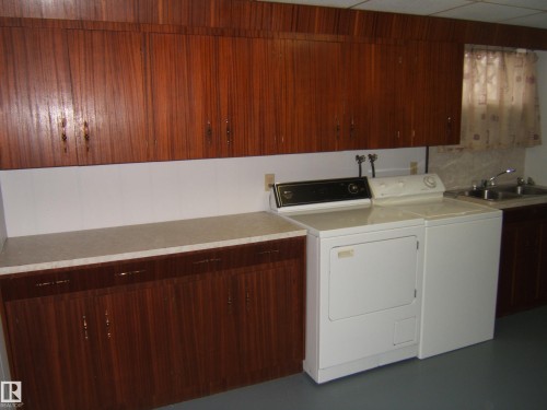 Laundry area with extensive wood-finish cabinetry, light-toned countertops, and a double basin stainless steel sink - 5030 52 Avenue, Andrew, AB - Indoor Photo Showing Laundry Room