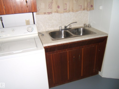 Utility area featuring a double basin sink with a laminate countertop, wood-finish cabinetry, and an overhead wood-finish cabinet - 5030 52 Avenue, Andrew, AB - Indoor Photo Showing Laundry Room