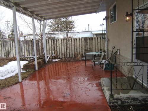 Covered patio featuring a red-finished concrete surface and a partial privacy fence - 5030 52 Avenue, Andrew, AB - Outdoor With Deck Patio Veranda