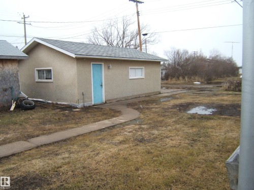Detached outbuilding with an asphalt shingle roof, stucco siding, and a light blue door - 5030 52 Avenue, Andrew, AB - Outdoor