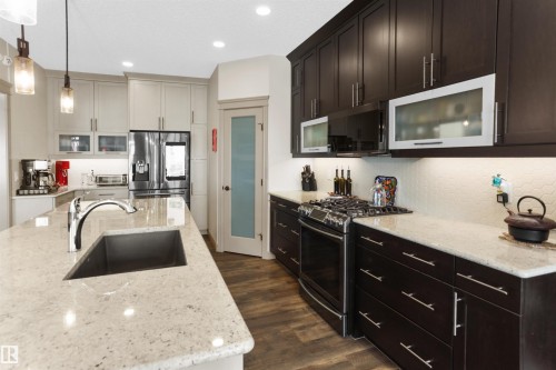 Kitchen featuring a large island with an undermount sink, light-toned countertops, contrasting dark and light cabinetry, stainless steel appliances, and wood-finish flooring - 97 Astoria Point(E), Devon, AB - Indoor Photo Showing Kitchen With Upgraded Kitchen