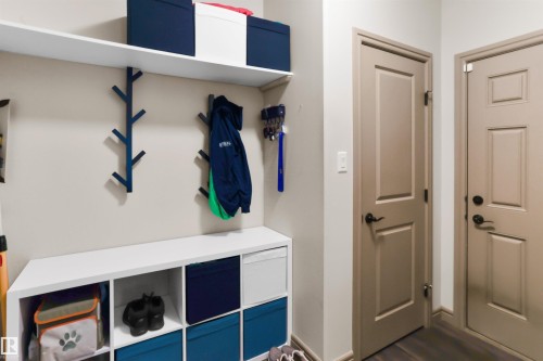 Dedicated entry organization area featuring a white built-in storage unit with cubbies, an overhead shelf, multiple wall-mounted coat hooks, two panel doors with dark hardware, and wood-finish flooring - 97 Astoria Point(E), Devon, AB - Indoor Photo Showing Other Room