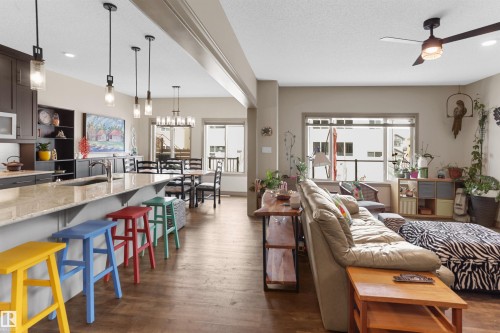 Open-concept living space featuring wood-finish flooring, a kitchen island with seating, dark wood cabinetry, a dining area with a contemporary chandelier, and recessed lighting - 97 Astoria Point(E), Devon, AB - Indoor