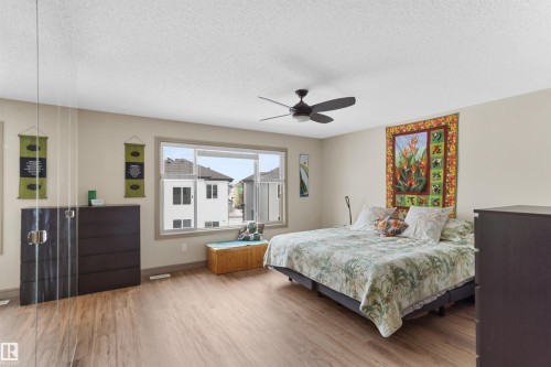 Spacious room featuring wood-finish flooring, a contemporary ceiling fan, and large windows providing abundant natural light - 97 Astoria Point(E), Devon, AB - Indoor Photo Showing Bedroom