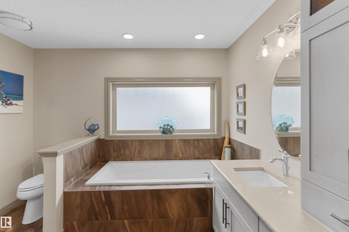 Soaking tub with surrounding wood-look tile, complemented by a large privacy window - 97 Astoria Point(E), Devon, AB - Indoor Photo Showing Bathroom