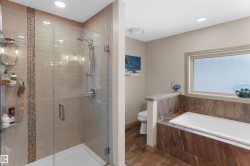 Spacious bathroom featuring a glass-enclosed shower with subway tile surround and mosaic accent, alongside a built-in soaking tub with stone-finish paneling and an opaque window - 