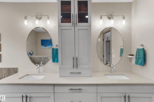 Double vanity featuring light-toned countertops, two undermount sinks, and separate oval mirrors - 97 Astoria Point(E), Devon, AB - Indoor Photo Showing Bathroom
