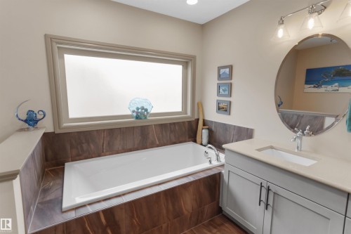 Bathroom featuring a built-in soaking tub with chrome fixtures, a frosted window, and wood-finish tile surround - 97 Astoria Point(E), Devon, AB - Indoor Photo Showing Bathroom