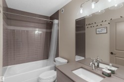 Bathroom featuring a neutral tile shower surround with a white tub, an integrated sink vanity with a polished chrome faucet, and overhead bar lighting - 