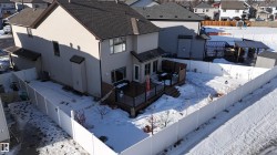 Expansive fenced backyard featuring a multi-level wooden deck with glass panel railings, a separate covered patio structure, and a storage shed - 